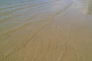 The waves beat at the beach with sand and reflection of sunlight in summer morning. Nature background concept.
