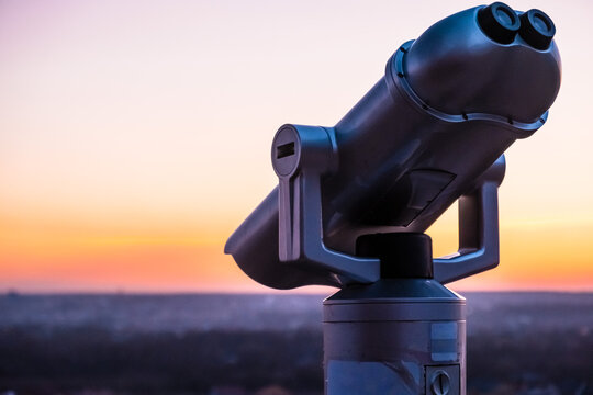 Observation deck and binoculars with a view of the city. Coin operated telescope binocular for sightseeing. Sunset above the european city from the viewing point