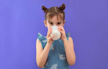 The child drinks milk with pleasure. Cute little girl with a glass of milk on a purple background. The concept of healthy eating