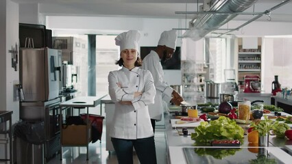 Portrait of confident woman posing with arms crossed in busy kitchen, preparing food recipe and gourmet meal for restaurant menu. Professional cook in uniform using ingredients to make organic dish.