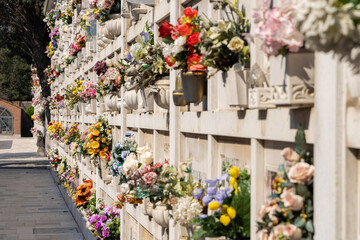 Fototapeta na wymiar Italian wall cemetery with tombstones and artificial flowers on a sunny summer day in Venice, Italy, Island of San Michele. Commemoration of the dead, deaths of pandemic.