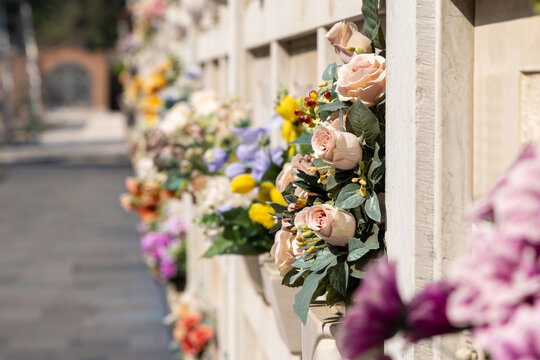 Italian wall cemetery with tombstones and artificial flowers on a sunny summer day in Venice, Italy, Island of San Michele. Commemoration of the dead, deaths of pandemic.
