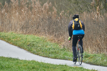 Radfahrer in Winterbekleidung und mit Rucksack auf einem Rennrad unterwegs auf dem Lahn-Radweg