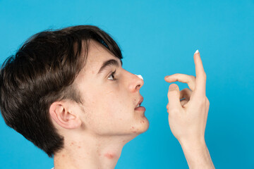 Obraz premium Side view of teenager boy with acne applying cream on face