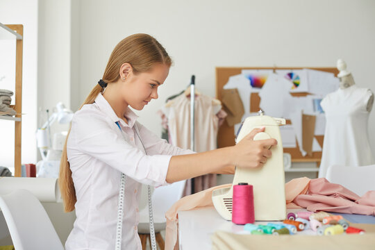 Woman seamstress work at sewing machine with fabric design garment in own small fashion atelier. Female designer or tailor cerate clothing pieces in workshop. Style, dressmaking concept.