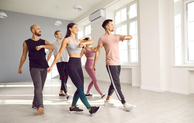 Group of fit young people doing physical exercises with a fitness instructor at the gym. Team of happy men and women enjoying an aerobics or sports dance workout class with a professional teacher