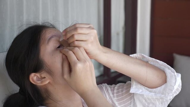 Close up of a middle-aged Asian woman looking up, applying single-dose medicine, dripping artificial tears to the eyes, at outdoors. Allergy and dry eyes problem concept.
