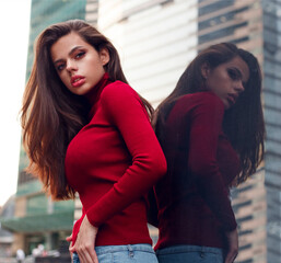 Beauty portrait of a sensual sexy girl in a fashionable red sweater posing on the street near a wall. reflection