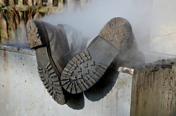 repair piping with hot water steam in hatch of device. only shoes and feet look out of tank. smoke rolls in winds which rolls fog, dust. stainless steel kitchen equipment washes inside men, film, army