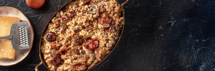 Risotto ai funghi panorama, mushroom rice with cheese, shot from above on a black background with copy space