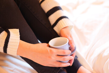 ベッドの上でコーヒーカップを持つ女性