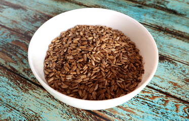 Whole unpeeled milk thistle seeds in a white bowl on an old shabby wooden background. Hepatoprotector for liver restoration.