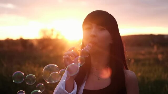 pretty young woman making soap bubbles in summer green field on sunset. happy peaceful time. millennial generation.