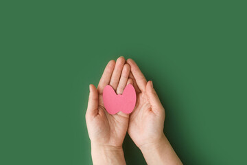 World Thyroid Day. Adult hands holding paper form of thyroid gland on green background. Problems with thyroid. Polycystic disease. World cancer day. copy space. banner