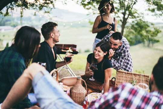 Happy friends having fun drinking wine at picnic dinner outdoor - Focus on center girl face