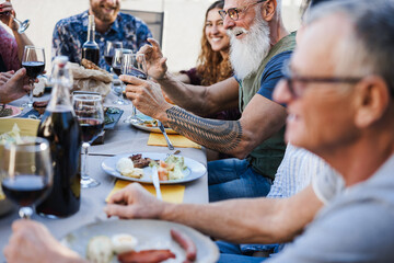 Family people eating at barbecue dinner outdoor - Focus on senior hand holding glass of wine
