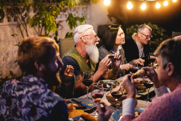 Happy multiracial family people eating at barbecue dinner outdoor - Focus on senior man face