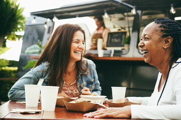 Happy multiracial senior women eating at food truck restaurant outdoor - Focus on african female face