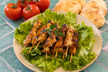 grilled chicken skewers on lettuce leaves , fresh ripe tomatoes and bread on table