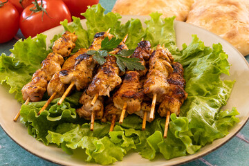 grilled chicken skewers on lettuce leaves , fresh ripe tomatoes and bread on table