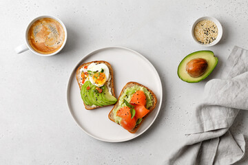 Two avocado sandwiches with salmon, eggs, basil, micro greens. White plate and cup of coffee