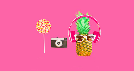 Fashion pineapple with headphones, sunglasses, lollipop caramel on stick and film camera on colorful pink background