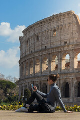Young man using smartphone and sitting resting in the coliseum in Rome, Italy