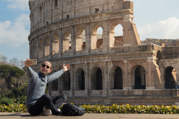 Young man making a video call while visiting the coliseum in Rome - obrazy, fototapety, plakaty
