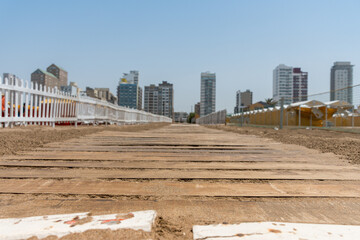 Selective focus of a wooden pathway on the beach with city buildings in the background
