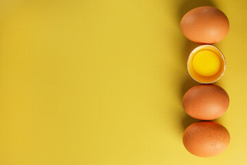 Fresh brown eggs and a broken egg with yolk on a light yellow background with space for text, copy space