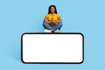 Cheerful african american woman showing namaste gesture, sitting on smartphone