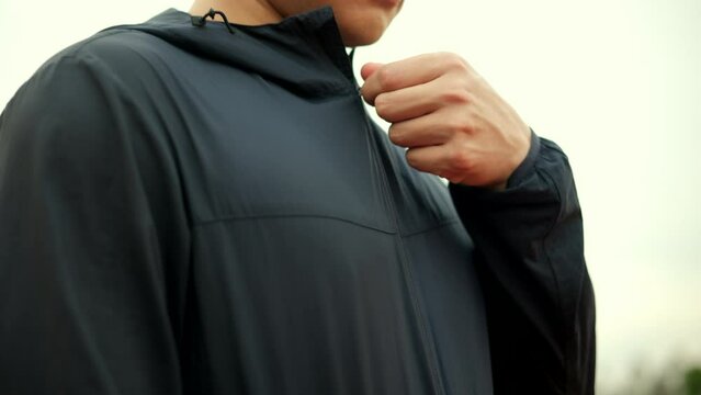 Close up hand asian man zipping wearing sportswear dark blue jacket standing with arms crossed on track stadium running outdoor.  Chinese man jogging on the road. Training athlete outdoor concept.