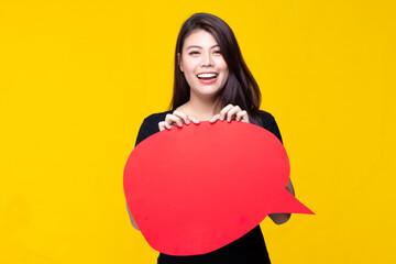 Attractive beautiful young asian woman smile and excited holding empty speech bubble isolated on yellow background.