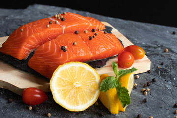 Salmon. Fresh raw salmon fish. Raw salmon fillet with pepper, herbs, lemon, tomato ingredients for cooking on black stone table rustic style. Top view with copy space.