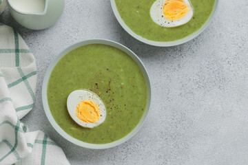 Spinach green homemade cream soup with boiled egg, close up top view banner  on a gray neutral background with copy space, healthy food concept