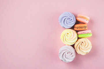 Traditional colored sweet desserts for the holiday, copy space. Desserts: macaroons, marshmallows and zephyrs on a pink background, closeup. Top view.