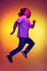 Fototapeta na wymiar Full-length portrait of young excited man jumping isolated on orange background in neon light, filter. Concept of emotions, beauty, fashion