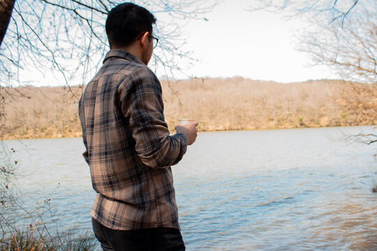 Man drinking tea and staring at lake, thinking person with cup of coffee in forest, lakeside and person with lumberjack shirt