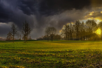 Landscape with heavy clouds and an impending storm with a bright sun and floodlight backlit over the hilly lawns of a golf course in Zegersloot Alphen aan den Rijn