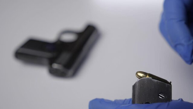 A hand in a blue glove loads a pistol clip. Killer. Police Investigator.