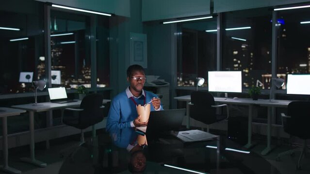 African-American employee work late in office and eat takeaway food with night city center view 