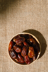 Dried dates in a wooden cup on a brown textile background. View from above. Rustic style