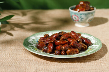 Dried dates in a green vintage plate on a brown textile background. Rustic style