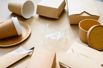 A crumpled disposable plastic cup lies with eco-friendly paper utensils. The concept of environmental protection. Selective focus in the center on a plastic cup.