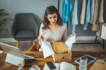 Excited caucasian young woman sit on chair at home unpack cardboard box shopping online, overjoyed black millennial girl buyer feel euphoric open shipped package parcel from delivery service