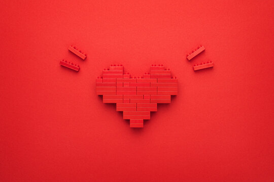 Flat lay image of like button on red background. Red heart symbol made of plastic building blocks. Top-down composition of toy pixelated heart model. Minimalist photo of stylized red love symbol.