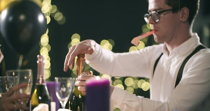 young attractive man removes a label from a bottle of champagne that would open with a pipe-tongue in his mouth. new year, Christmas, birthday