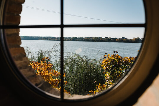 View through the round window to the lake. Sunset at the lake in autumn.