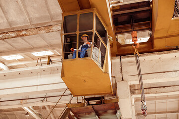 Male worker sitting in operator cabin of overhead crane - obrazy, fototapety, plakaty