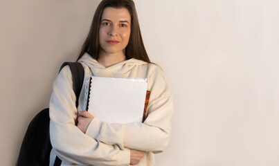 Student in trendy sweatshirts standing in hands holds notebooks on wall background with copy space